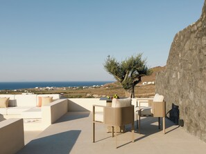 Une terrasse offrant une vue sur la mer, aménagée avec un canapé, des fauteuils et une table sur laquelle se trouve un saladier rempli de fruits.