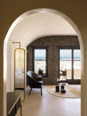 Une chambre à coucher avec un lit, une chaise, une table et une vue sur la plage par la fenêtre.