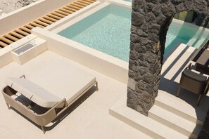 A pool area with a lounge chair, a stone pillar, and a small table. - Elysian Retreat (Santorini)