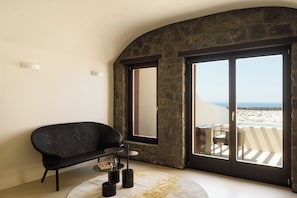 A modern room with a black sofa, a small round table, and a large window with a view of the beach.