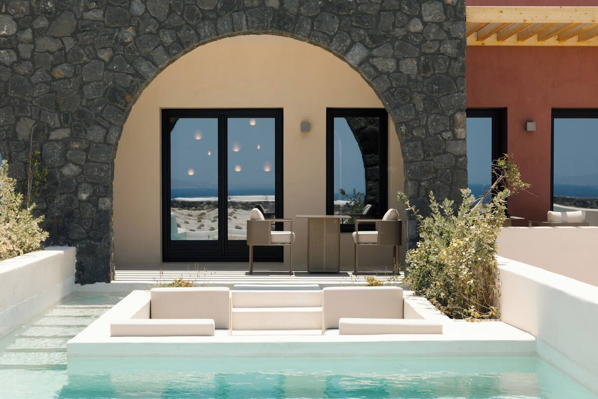 A pool area with stone walls, a seating area with chairs, and a view of the sea.