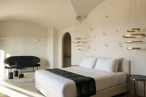 A modern hotel room with a large bed, a black sofa, a small round table, and a unique wall-mounted light fixture. - Elysian Retreat (Santorini)