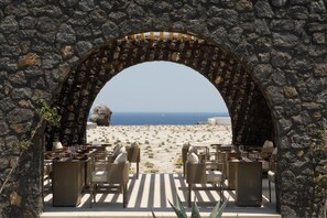 Ein Außenbereich mit Sitzgelegenheit, Steinmauern und Blick auf Strand und Meer.