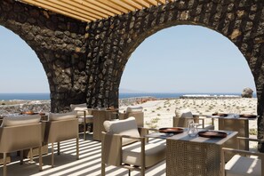 Une terrasse dotée de mobilier en osier, d’arches en pierre et offrant une vue sur la mer.