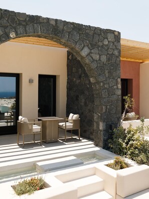 A stone archway leading to a patio with outdoor furniture and a view of the sea. - Elysian Retreat (Santorini)