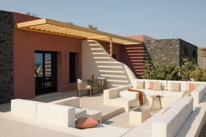 A modern outdoor seating area with white sofas and a wooden pergola. - Elysian Retreat (Santorini)