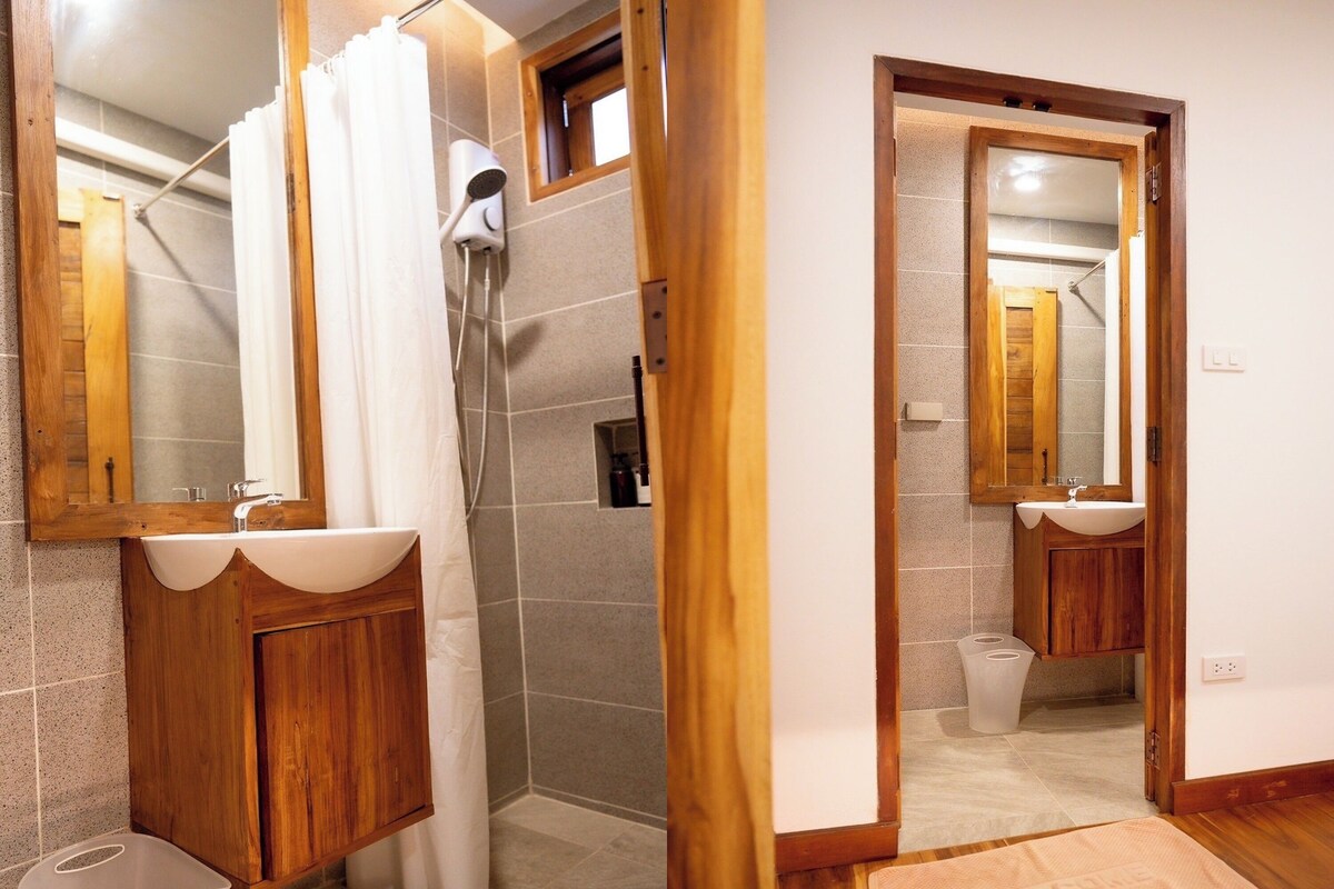 A bathroom with a wooden vanity, a shower, and a mirror.