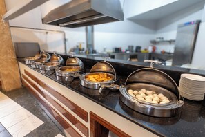 Una barra de buffet con diversos alimentos, incluyendo un bol de dumplings y un recipiente con aperitivos fritos.