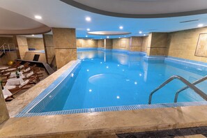 Una piscina interior con paredes de azulejos, una escalera de piscina y sillas de descanso con toallas.