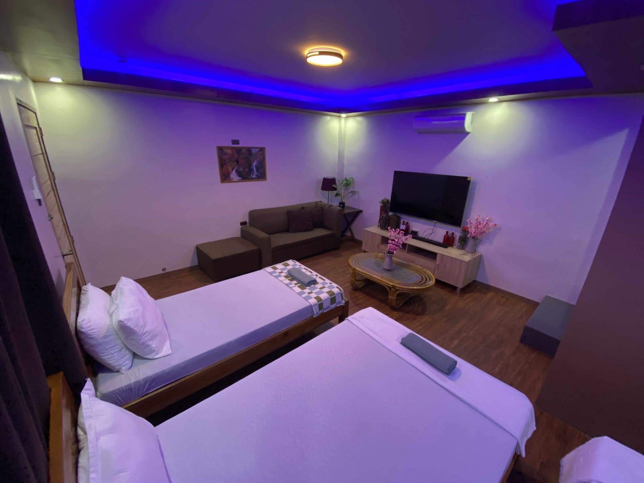 A hotel room with a bed, a sofa, a TV, and a small table with flowers.