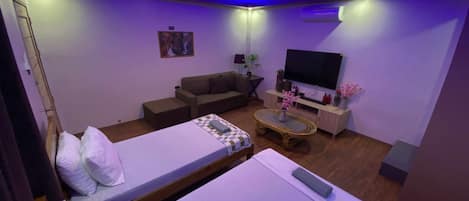 A hotel room with a bed, a sofa, a TV, and a small table with flowers.