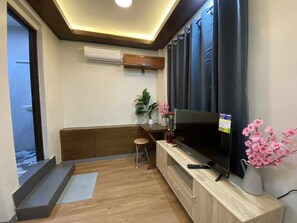 A room with a TV, wooden furniture, a small stool, a potted plant, and an air conditioning unit. - Mom Shies Apartelle and Restaurant (Caba)