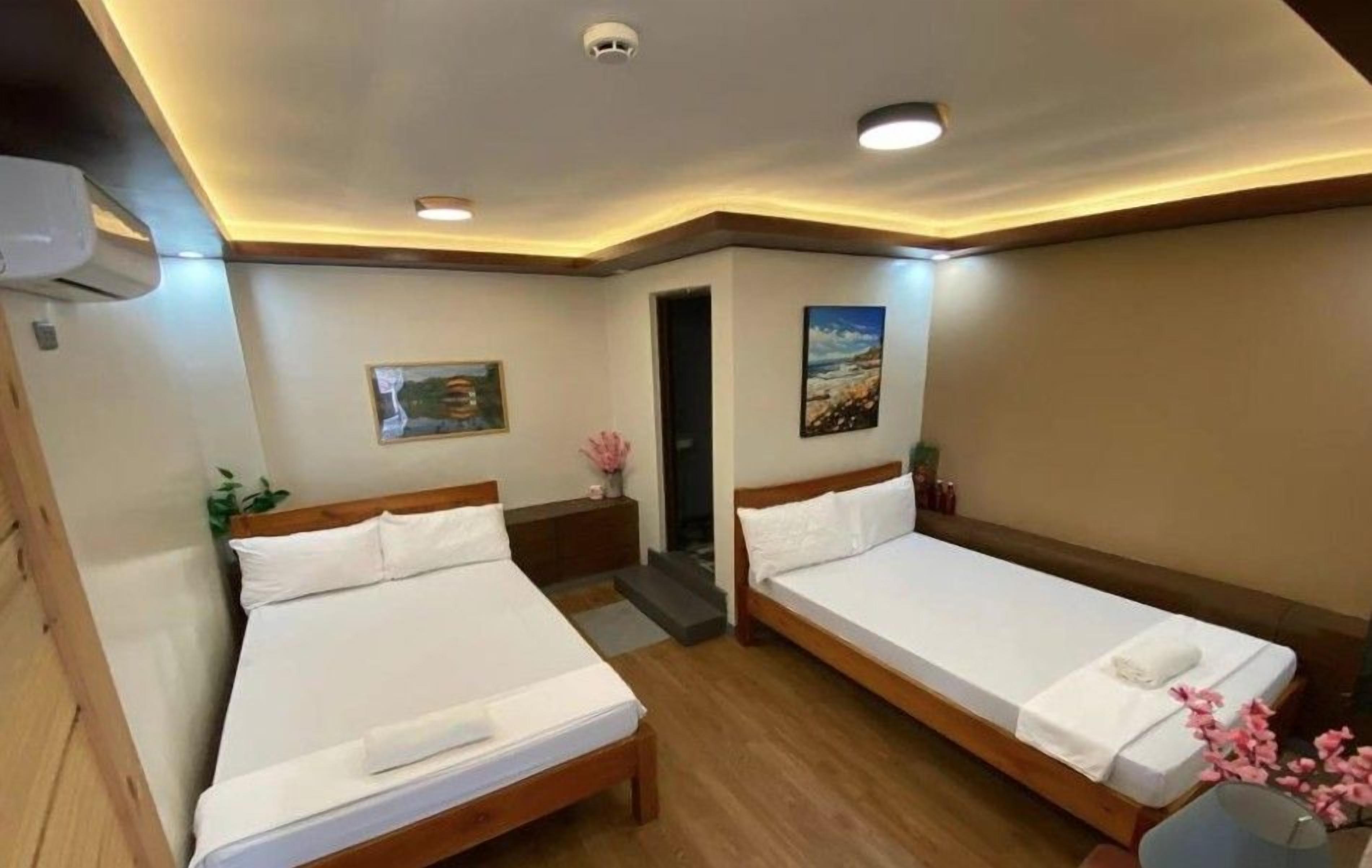A hotel room with two beds, a painting, a small table with a vase, and a door leading to another room.