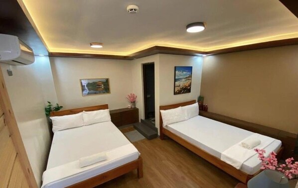 Ein Hotelzimmer mit zwei Betten, einem Gemälde, einem kleinen Tisch mit einer Vase und einer Tür zu einem anderen Raum.