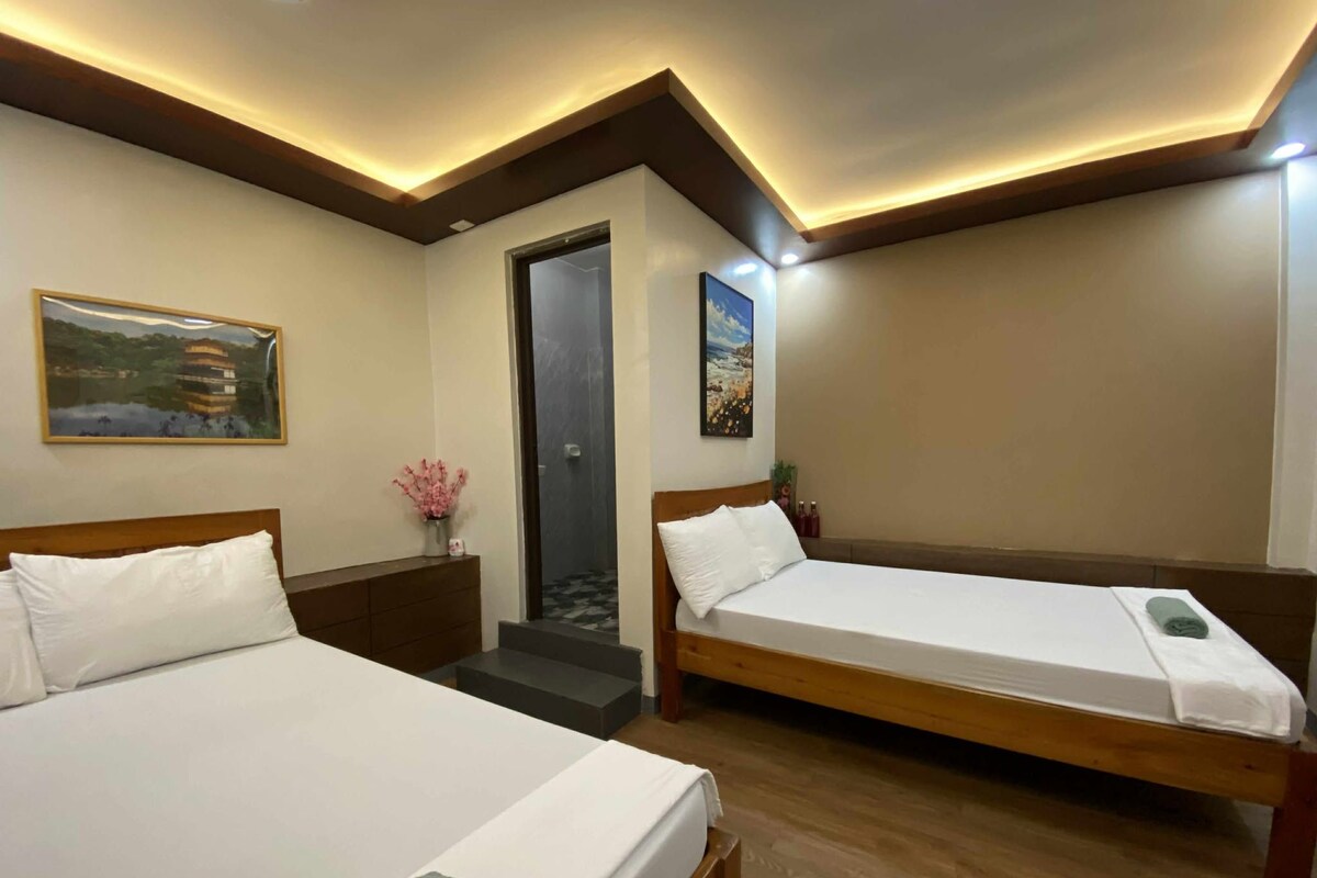 A hotel room with two beds, a wooden headboard, a small table with a vase of flowers, and a painting on the wall.