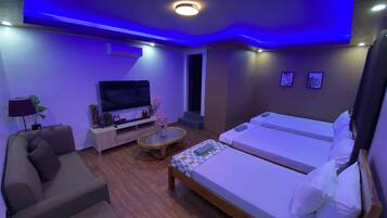 A hotel room with a sofa, a TV, a small table with a vase, two beds, and a ceiling light.