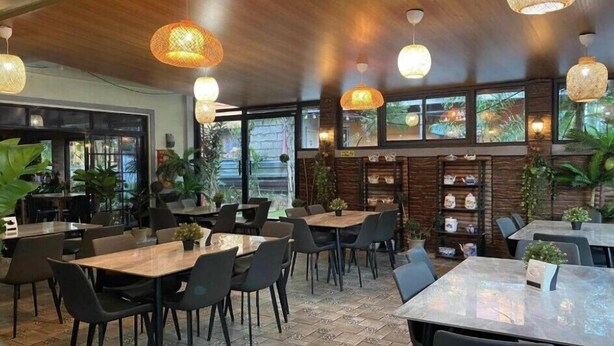 A restaurant with wooden tables and chairs, hanging wicker lamps, and large windows with views of greenery. - Mom Shies Apartelle and Restaurant (Caba)