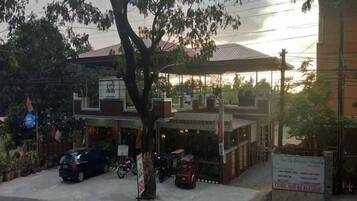 A building with a covered parking area, a tree in front, and a signboard.