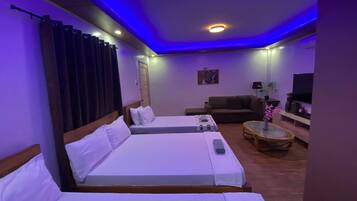A hotel room with two beds, a sofa, a TV, and a small table with a plant.