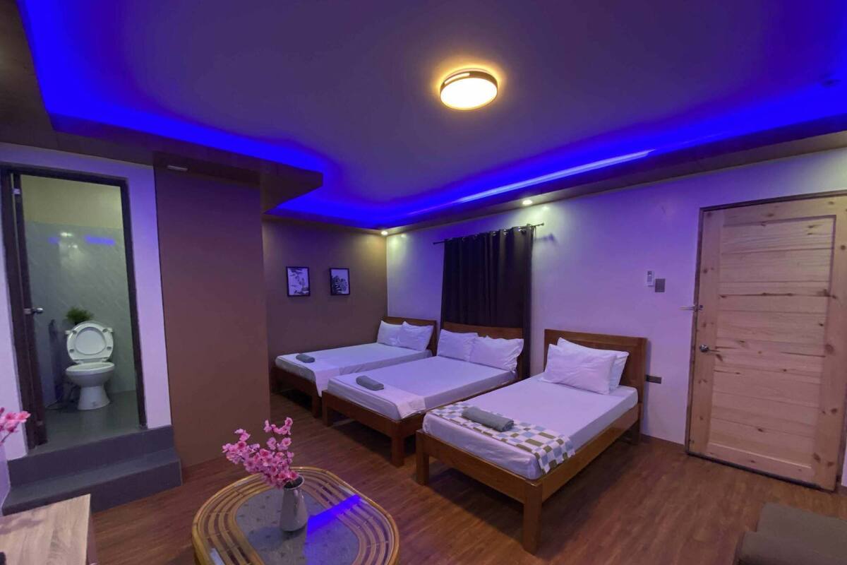 A hotel room with two single beds, a wooden door, a small table with a vase, and a bathroom visible through a glass partition.