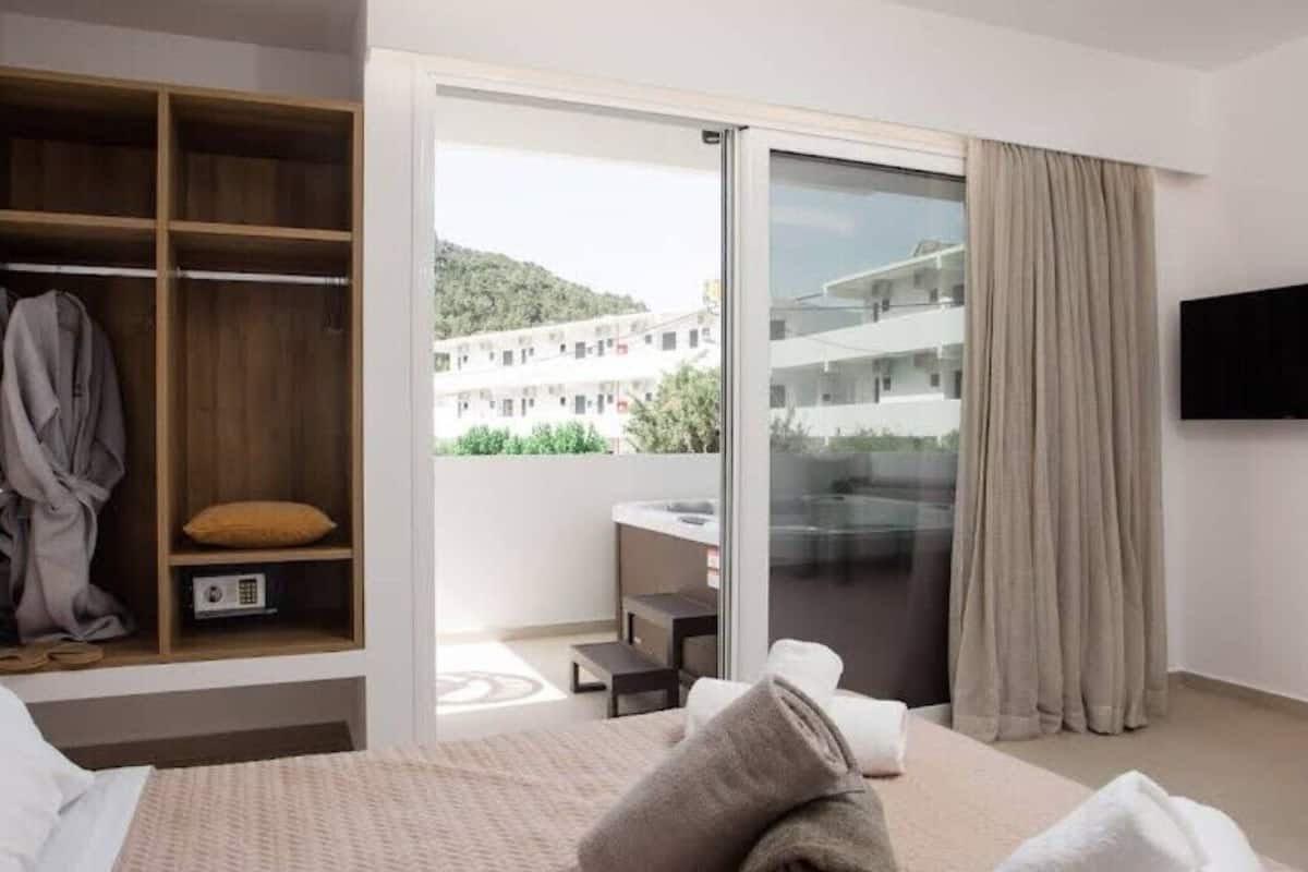 Une chambre d’hôtel comprenant un lit, une armoire, une porte-fenêtre coulissante donnant sur un balcon et un téléviseur fixé au mur.