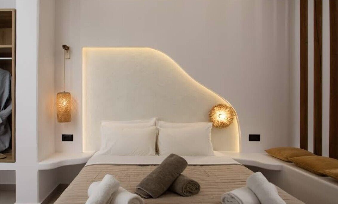 A modern bedroom with a curved headboard, a bedside lamp, and neatly folded towels.