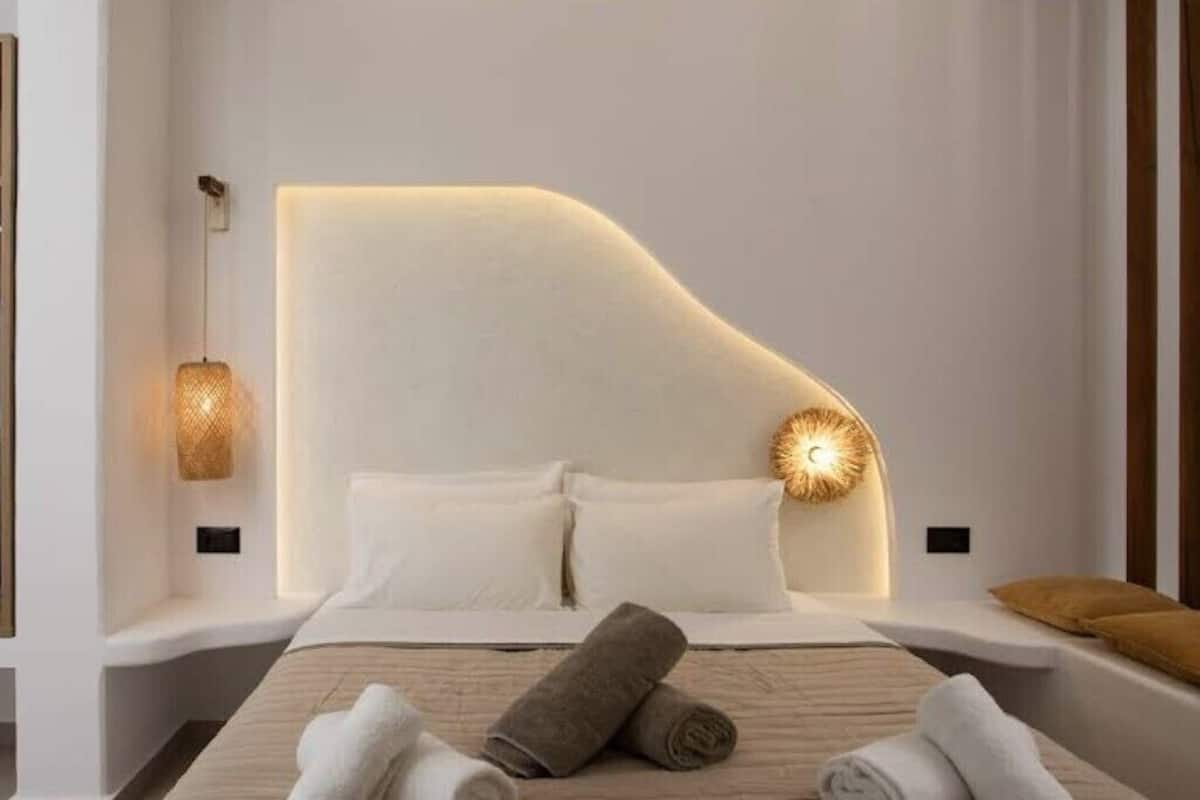 Une chambre à coucher moderne avec une tête de lit incurvée, une lampe de chevet et des serviettes soigneusement pliées.