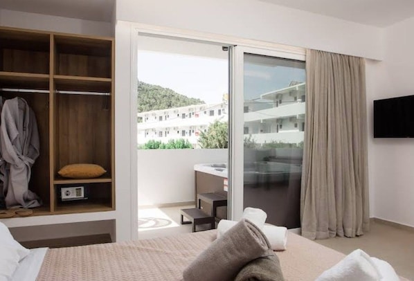 Habitación de hotel con cama, armario, puerta corrediza de vidrio a un balcón y televisor montado en la pared.