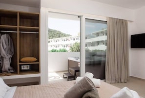 A hotel room with a bed, a wardrobe, a sliding glass door to a balcony, and a TV mounted on the wall. - Stay Helios (Rhodes)