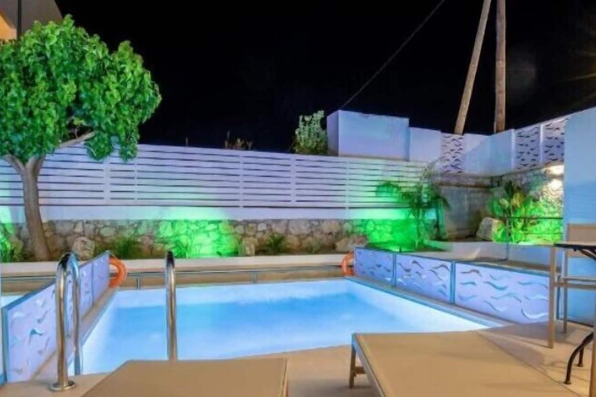 Une piscine avec une terrasse en bois, un arbre et un mur orné d’un motif texturé.