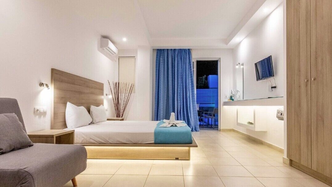 A modern hotel room with a bed, bedside table, a chair, a TV, and a bathroom with a mirror and sink.