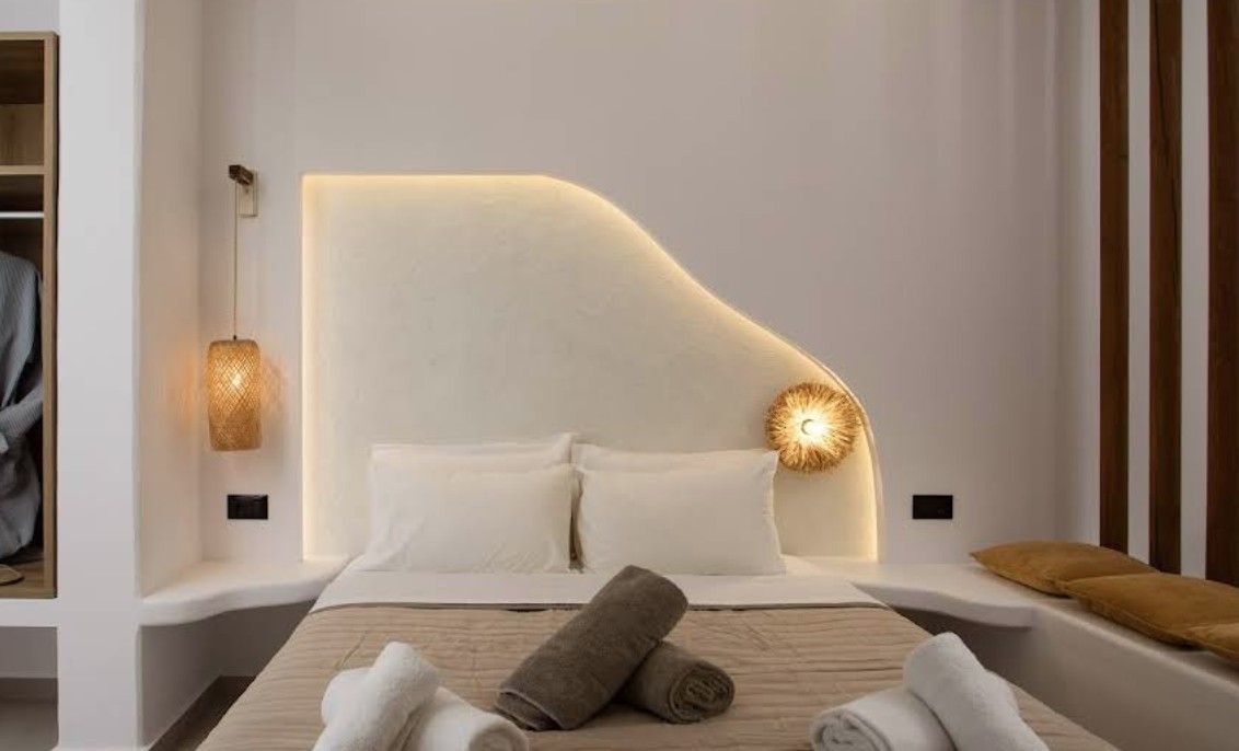 Un dormitorio moderno con cabecera curva, lámpara de noche y toallas dobladas con cuidado.