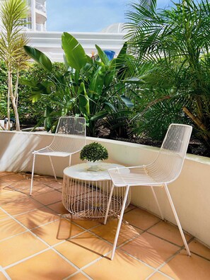 Eine Terrasse mit zwei weißen Stuhlgestellen, einem kleinen runden Tisch und einem Blumentopf.