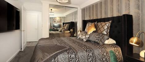 A bedroom with a large bed, a television, a mirror, and a modern chandelier.