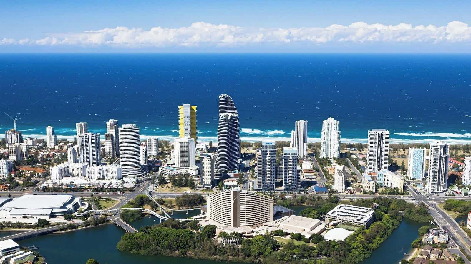A coastal cityscape with high-rise buildings, a marina, and a river.