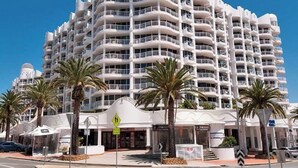 A multi-story hotel with balconies, palm trees, and a clear sky. - The Phoenician Luxe Suite (Broadbeach)