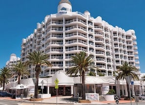 Ein mehrstöckiges Hotel mit Balkonen, Palmen und blauem Himmel.