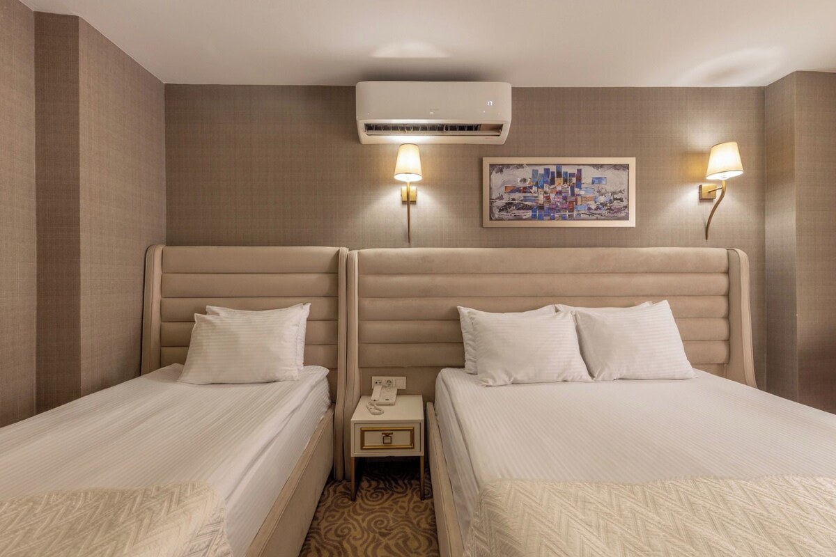 A hotel room with two beds, a nightstand, an air conditioning unit, and two wall-mounted lamps.