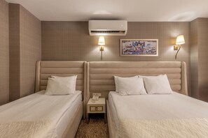 Une chambre d’hôtel avec deux lits, une table de chevet, un appareil de climatisation et deux lampes fixées au mur.