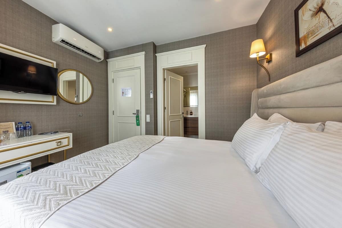 Ein Hotelzimmer mit einem Bett, einem Schreibtisch mit Spiegel, einem Fernseher und einer Klimaanlage.