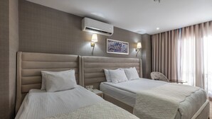 Habitación de hotel con dos camas, aire acondicionado de pared, dos lámparas de pared, un cuadro y una silla.