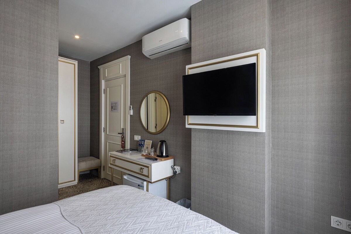 A hotel room with a bed, a dresser, a mirror, a television, and an air conditioning unit.
