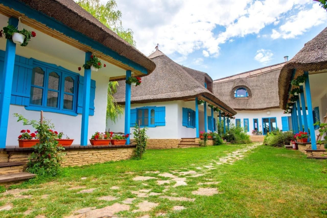 Eine Reihe traditioneller Häuser mit Strohdächern und blauen Fensterläden, angeordnet in einem Innenhof mit einem Steinweg.