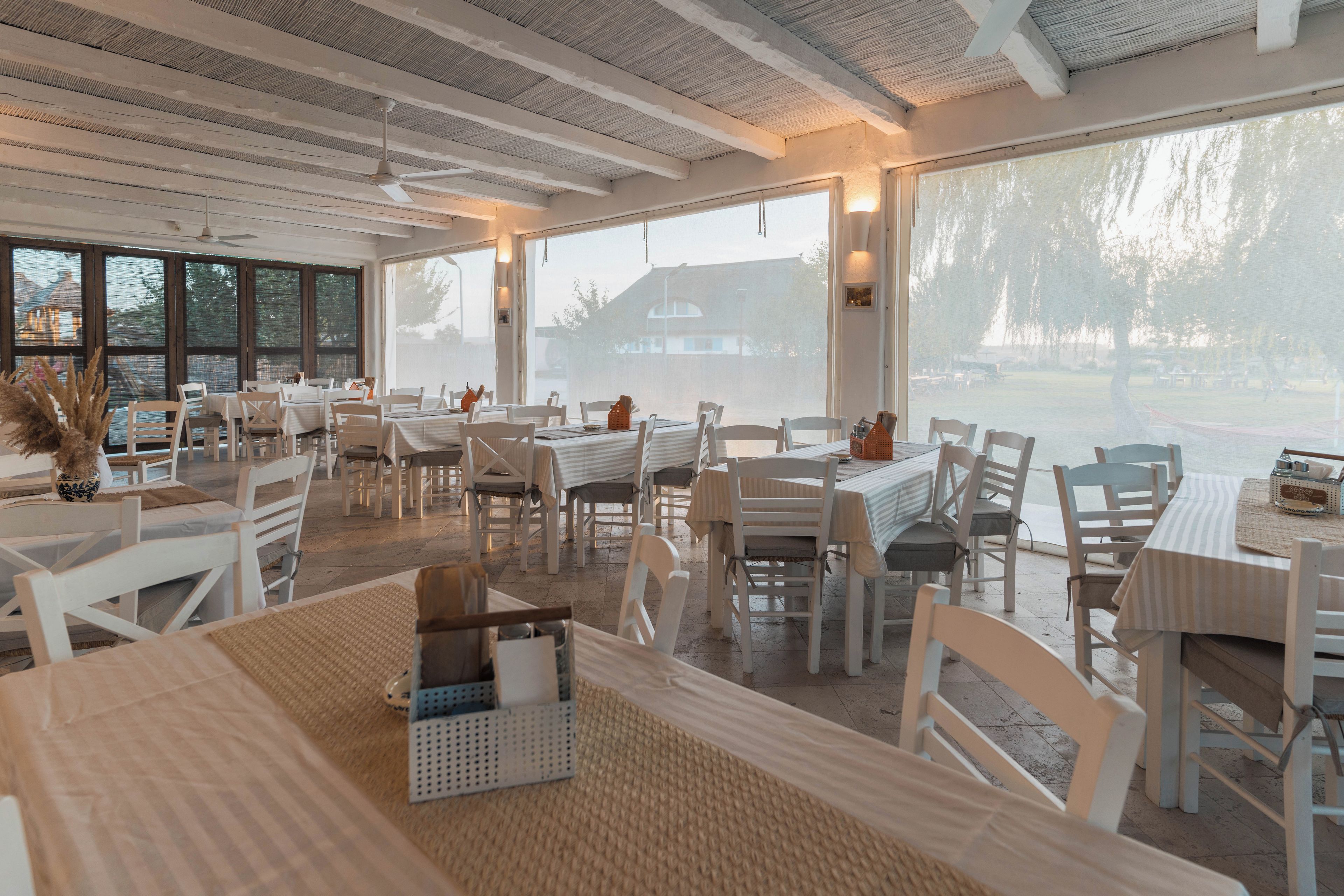 A spacious indoor dining area with large windows, white furniture, and a ceiling fan.