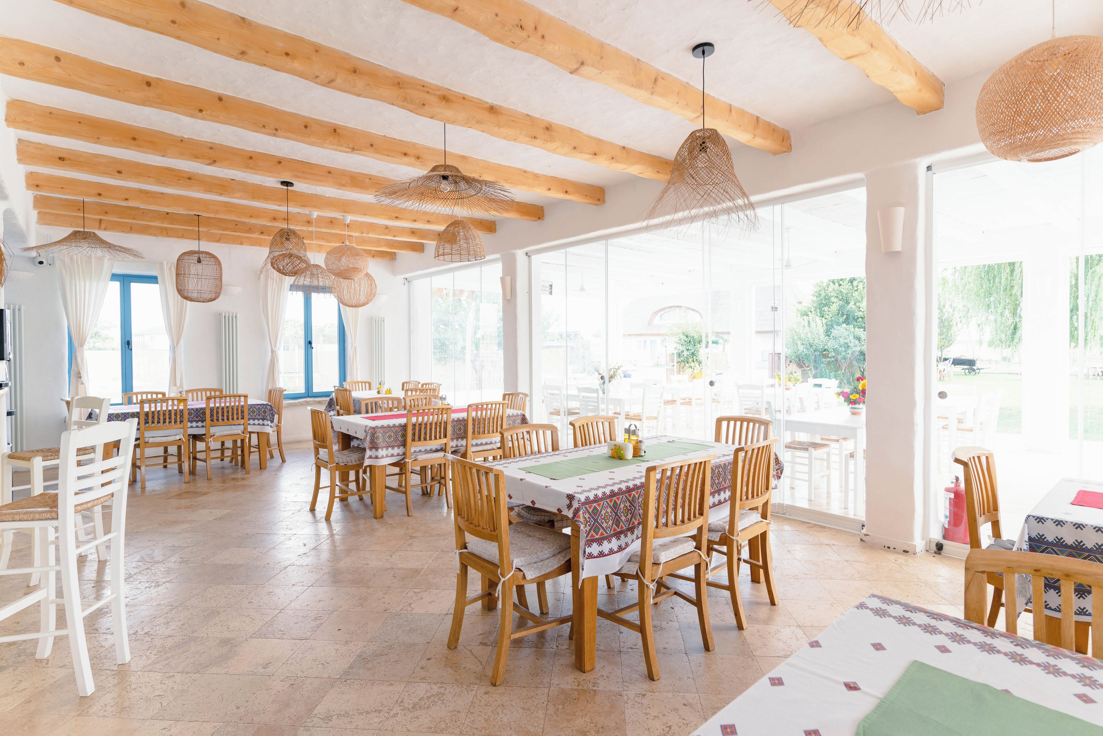 A spacious dining area with wooden tables and chairs, large windows, and hanging wicker lamps.