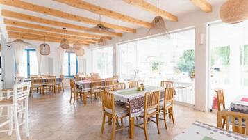 A spacious dining area with wooden tables and chairs, large windows, and hanging wicker lamps.