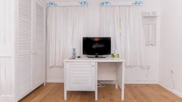A white desk with a television, a small vase, and a remote control.