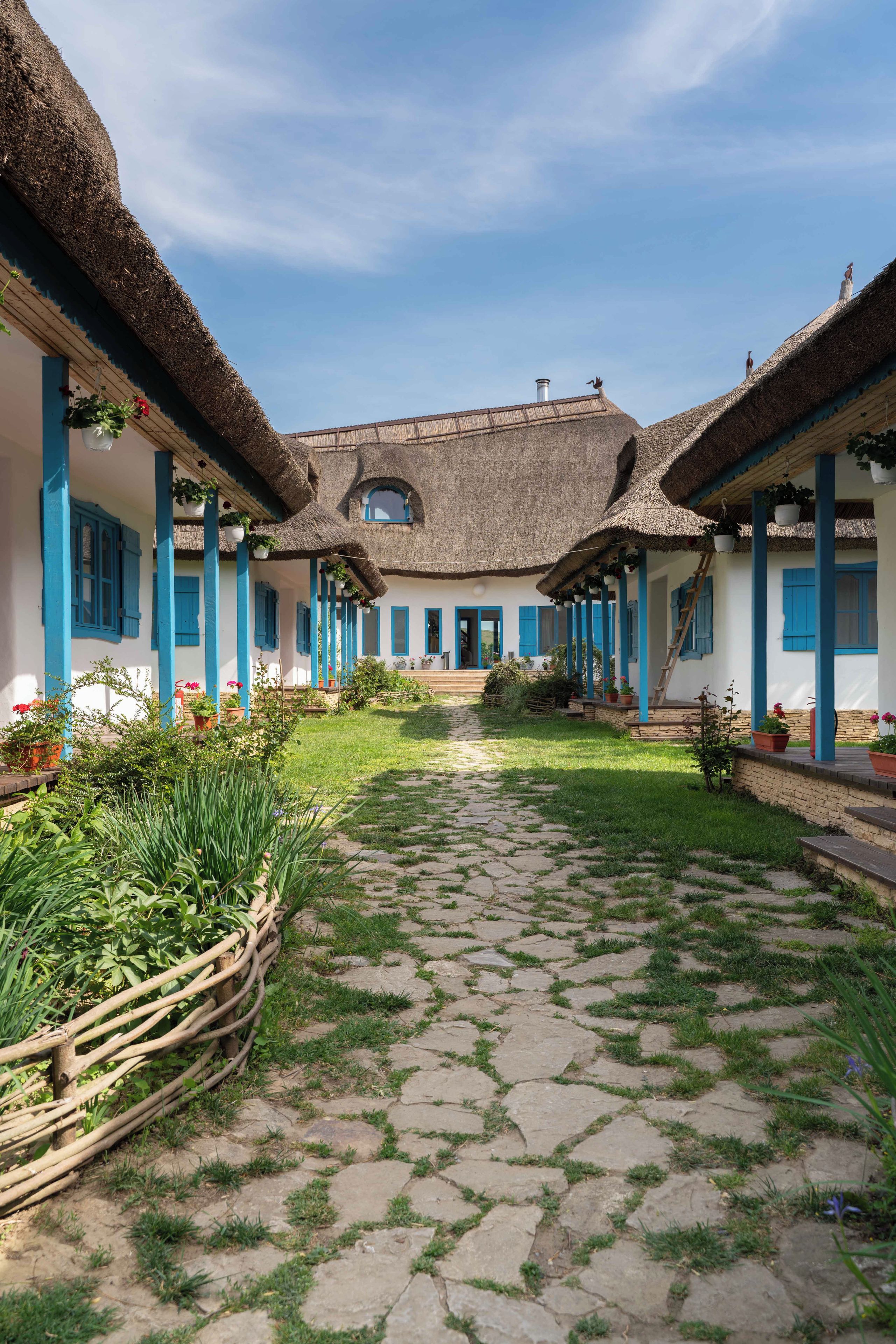 A traditional building with a thatched roof, blue shutters, and a central courtyard with a stone pathway.