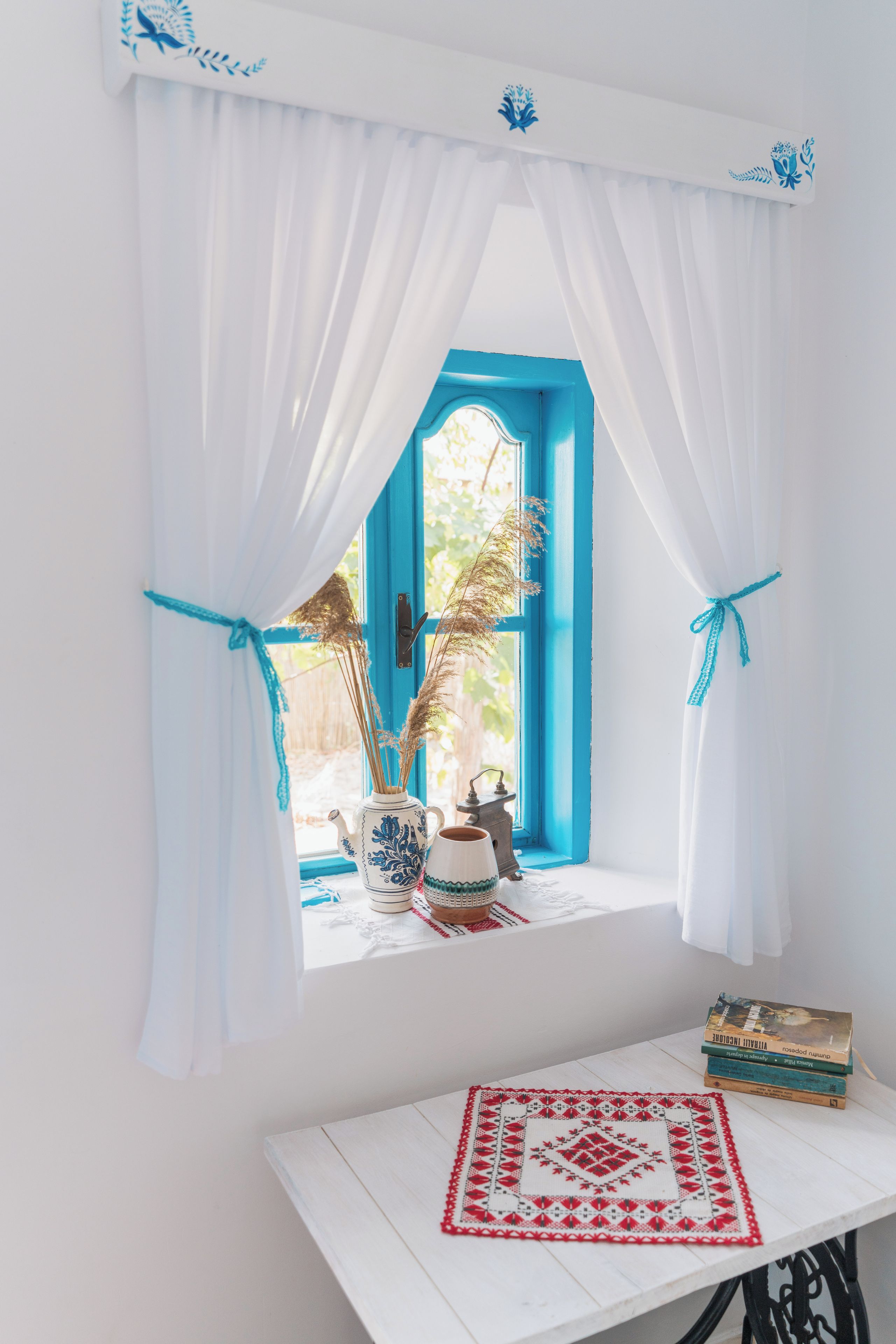 Una habitación con ventana, una mesa y un florero con plantas secas.