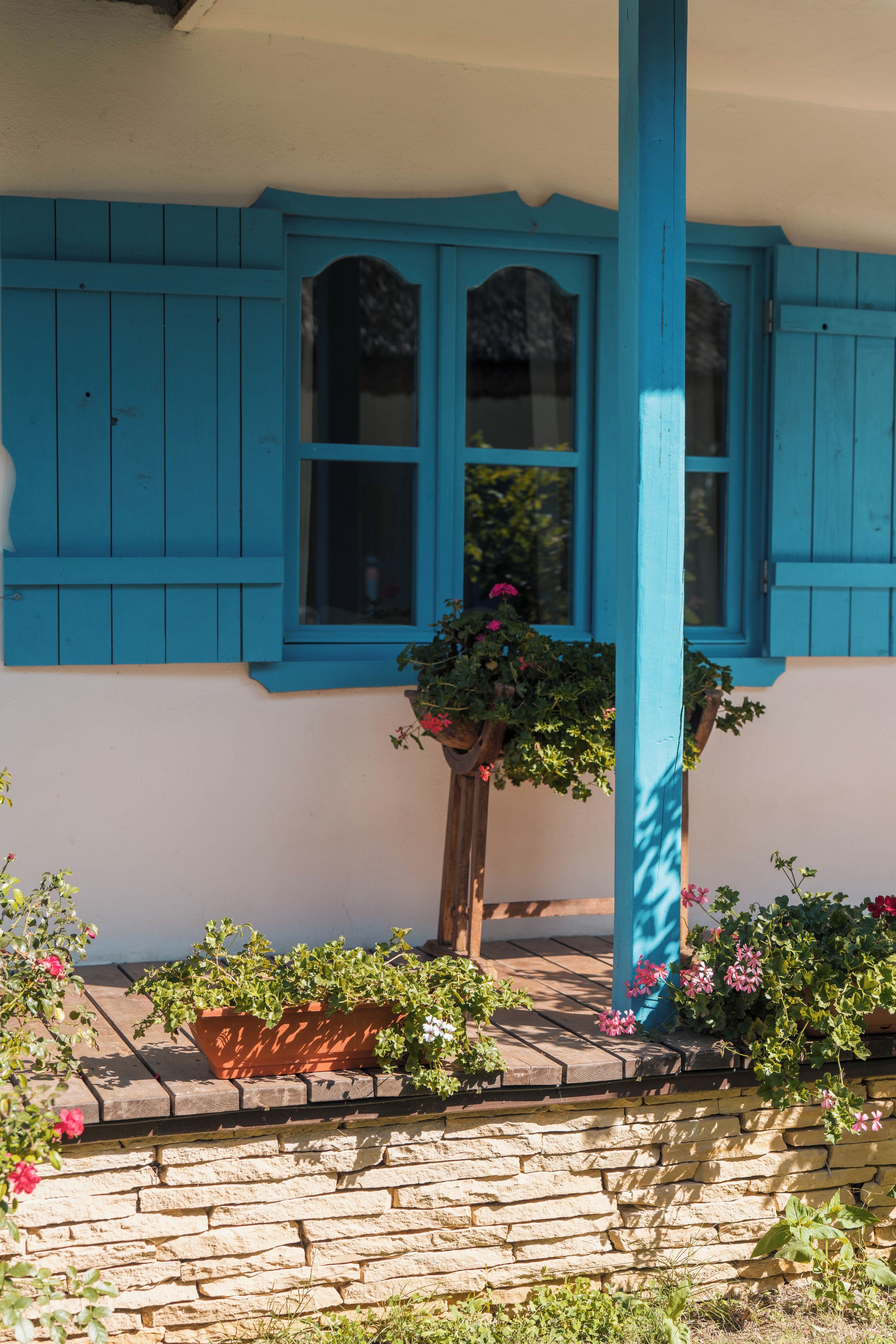 A building with blue shutters, a stone wall, and potted plants.